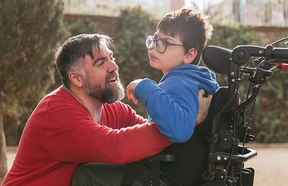 Loving father playing and enjoying time with his son with disability in a wheelchair.