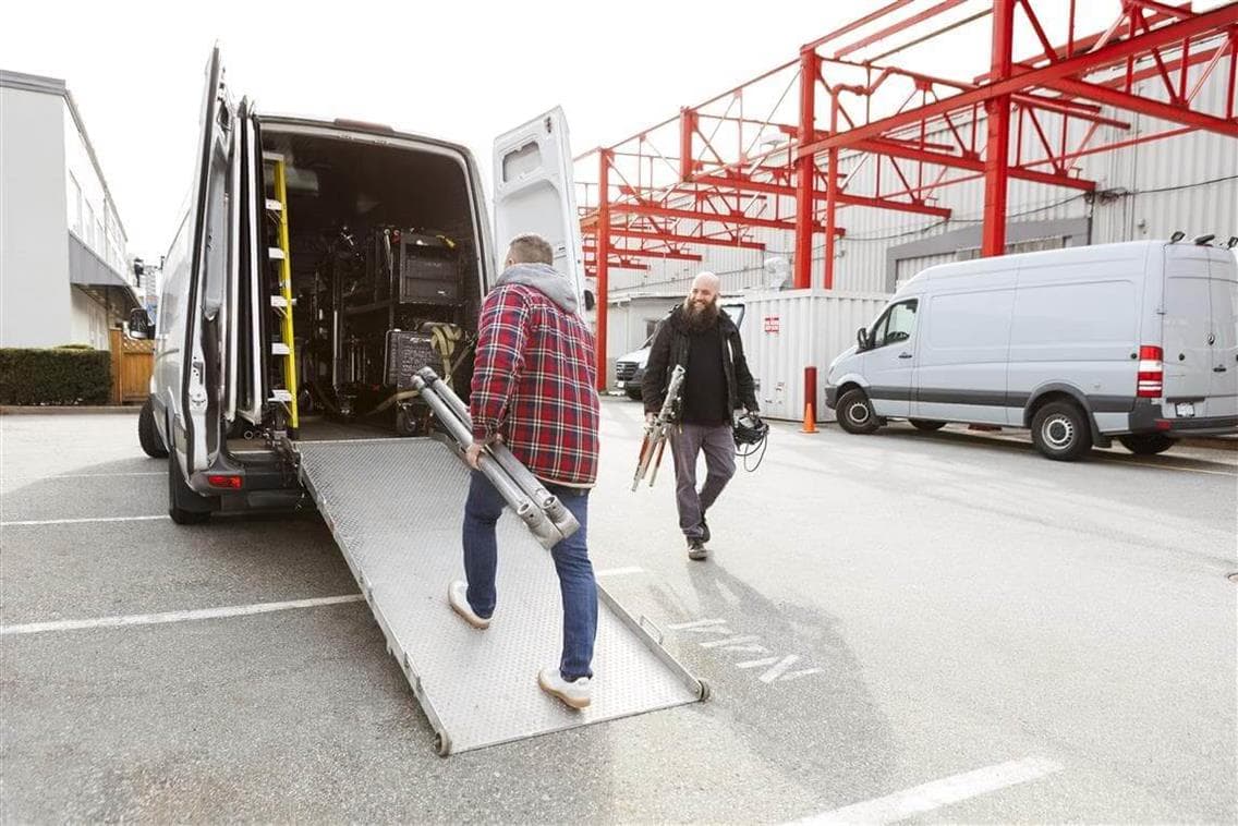 Two men keeping film production equipment in a van